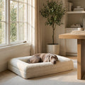 Dog resting on a cushion in a modern living room with a wooden table and chairs.
